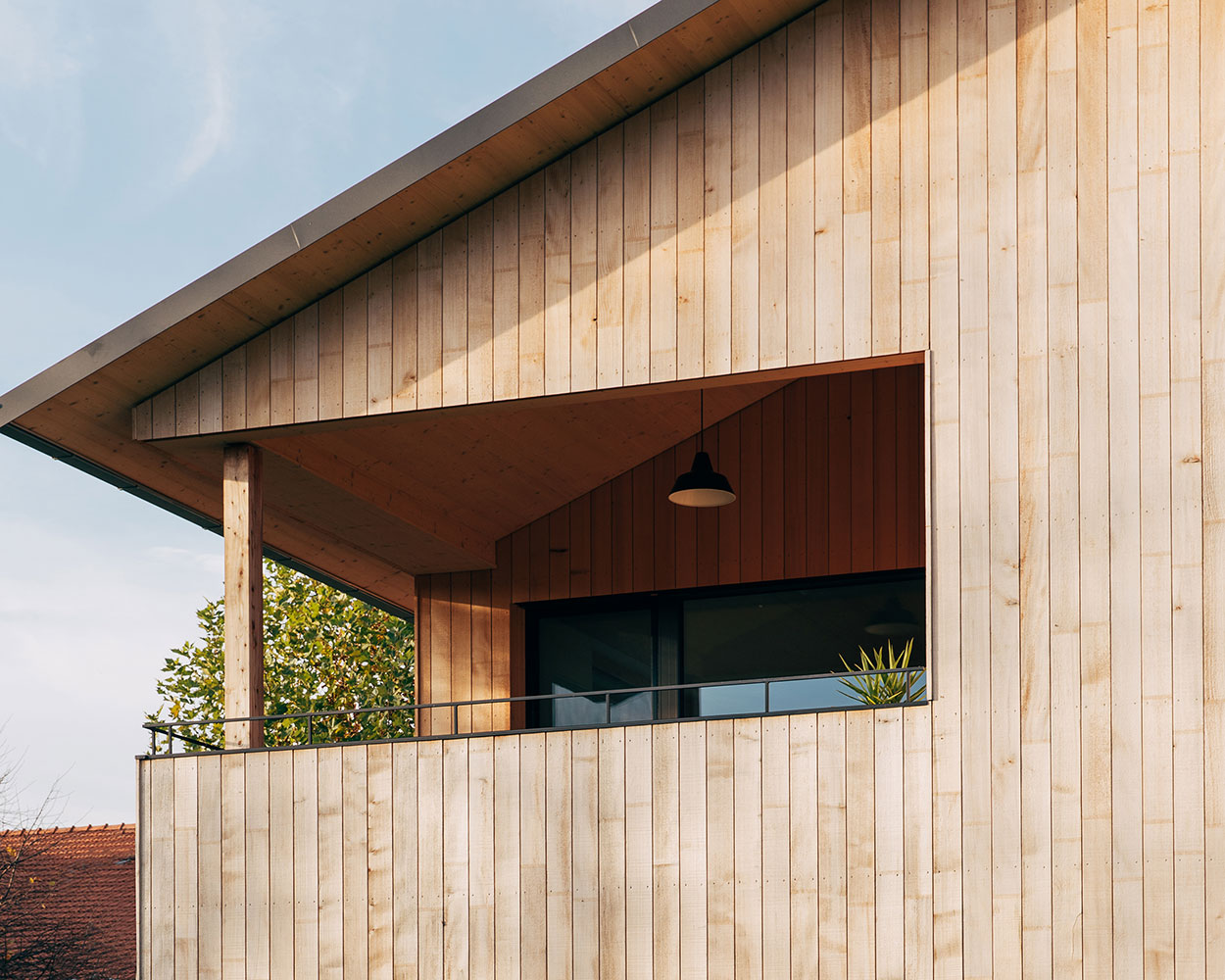 Ein modernes Holzhaus im Chiemgau zeigt einen überdachten Balkon mit stilvoller Außenbeleuchtung.