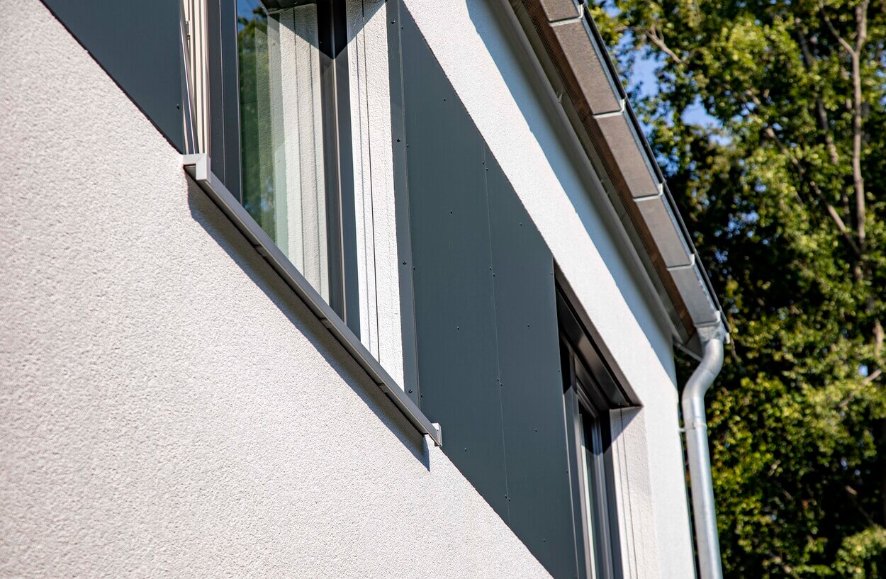 Detail der modernen Fassade eines Passivhauses in Eichenau mit schmalem Fenster und klaren Linien bei Sonnenschein.