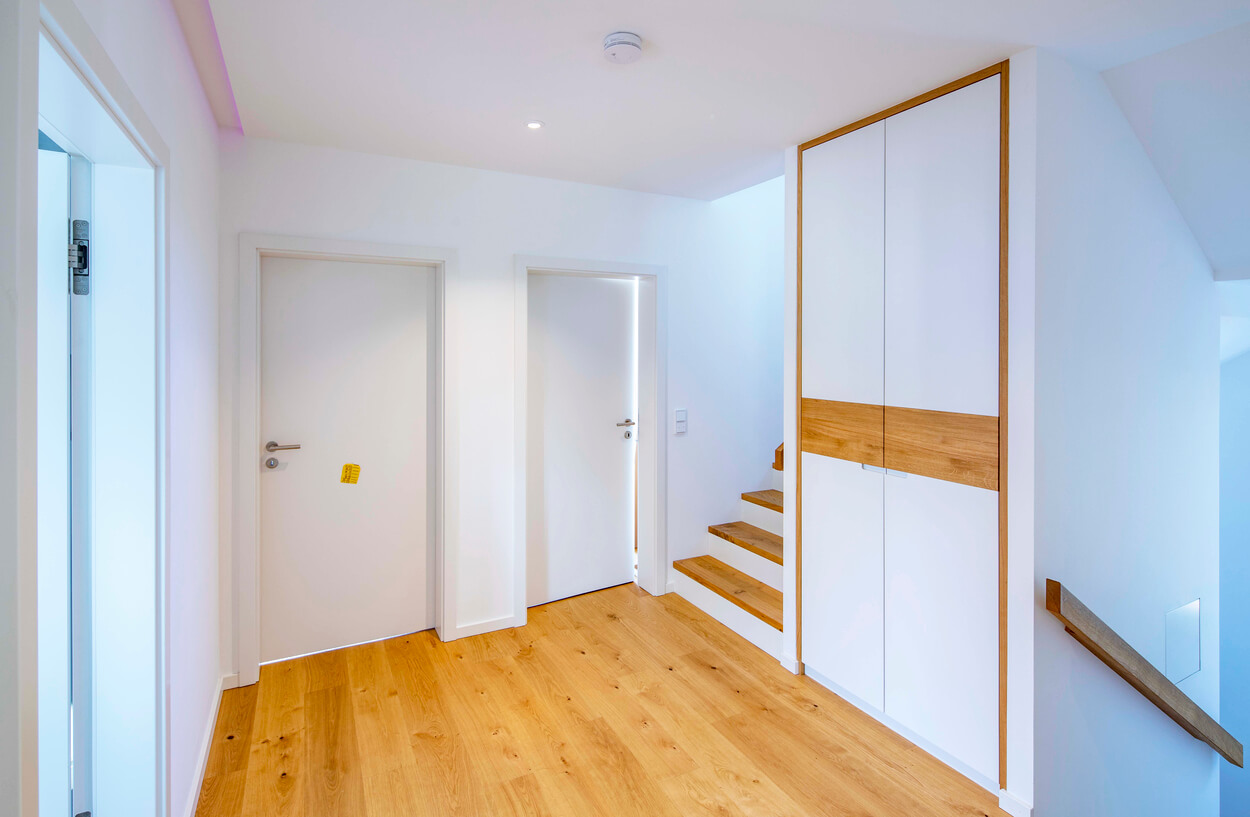 Ein moderner Flur in Eichenau zeigt einen Holzboden, weiße Türen und eine elegante Holztreppe im Passivhaus.