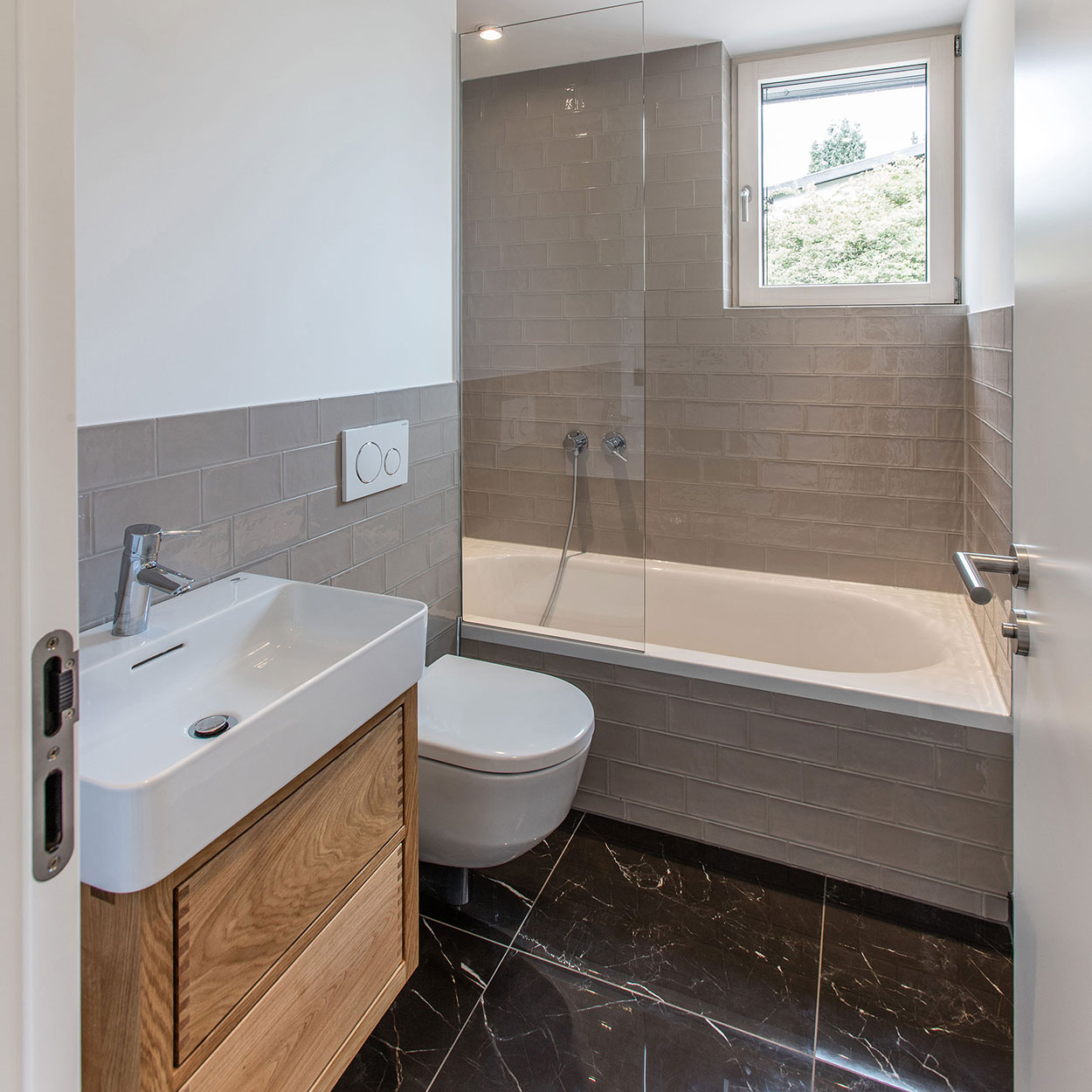 Modernes Badezimmer im Holzhaus mit grauen Fliesen, Holzschrank, Waschbecken, Toilette und Badewanne.