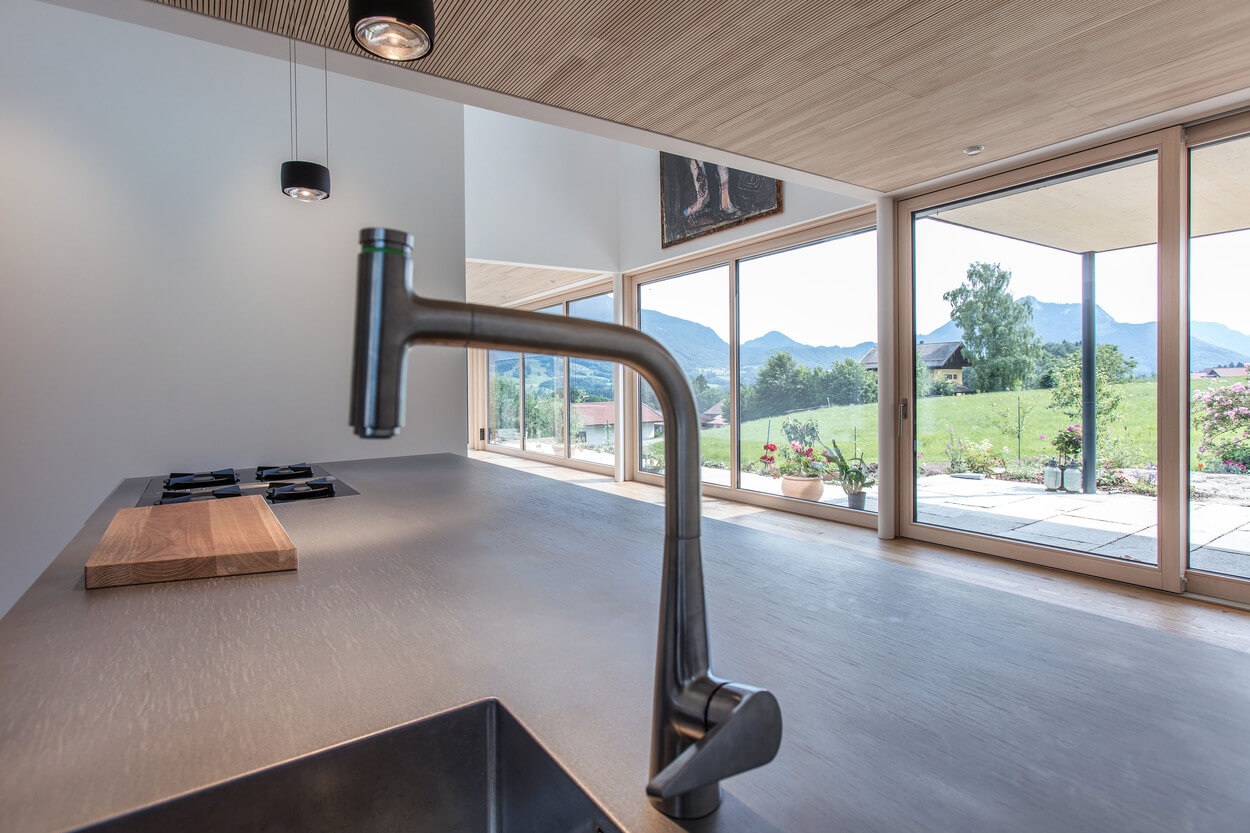 Moderne Küche in einem Holzhaus am Samerberg mit großem Fenster und herrlichem Bergblick.