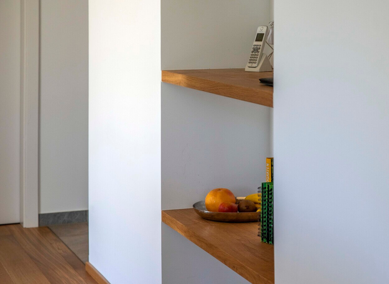 Ein Holzregal in einem Otterfinger Haus präsentiert ein Telefon, Notizbücher und bunte Früchte auf zwei Ebenen.