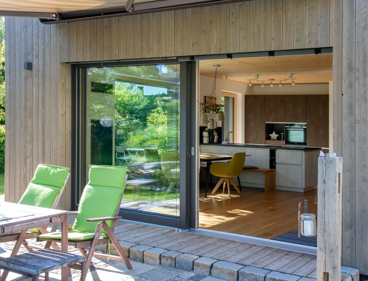 Eine Terrasse mit grünen Stühlen verbindet sich harmonisch mit der modernen Holzküche im Haus in Otterfing.