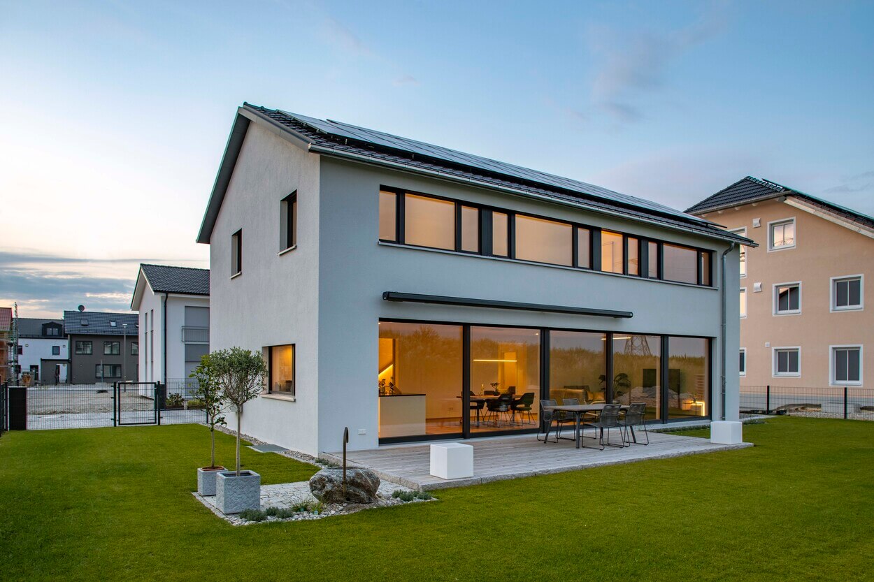 Ein modernes Passivhaus in Pliening mit großen Fenstern und gepflegtem Garten strahlt im Sonnenuntergang.