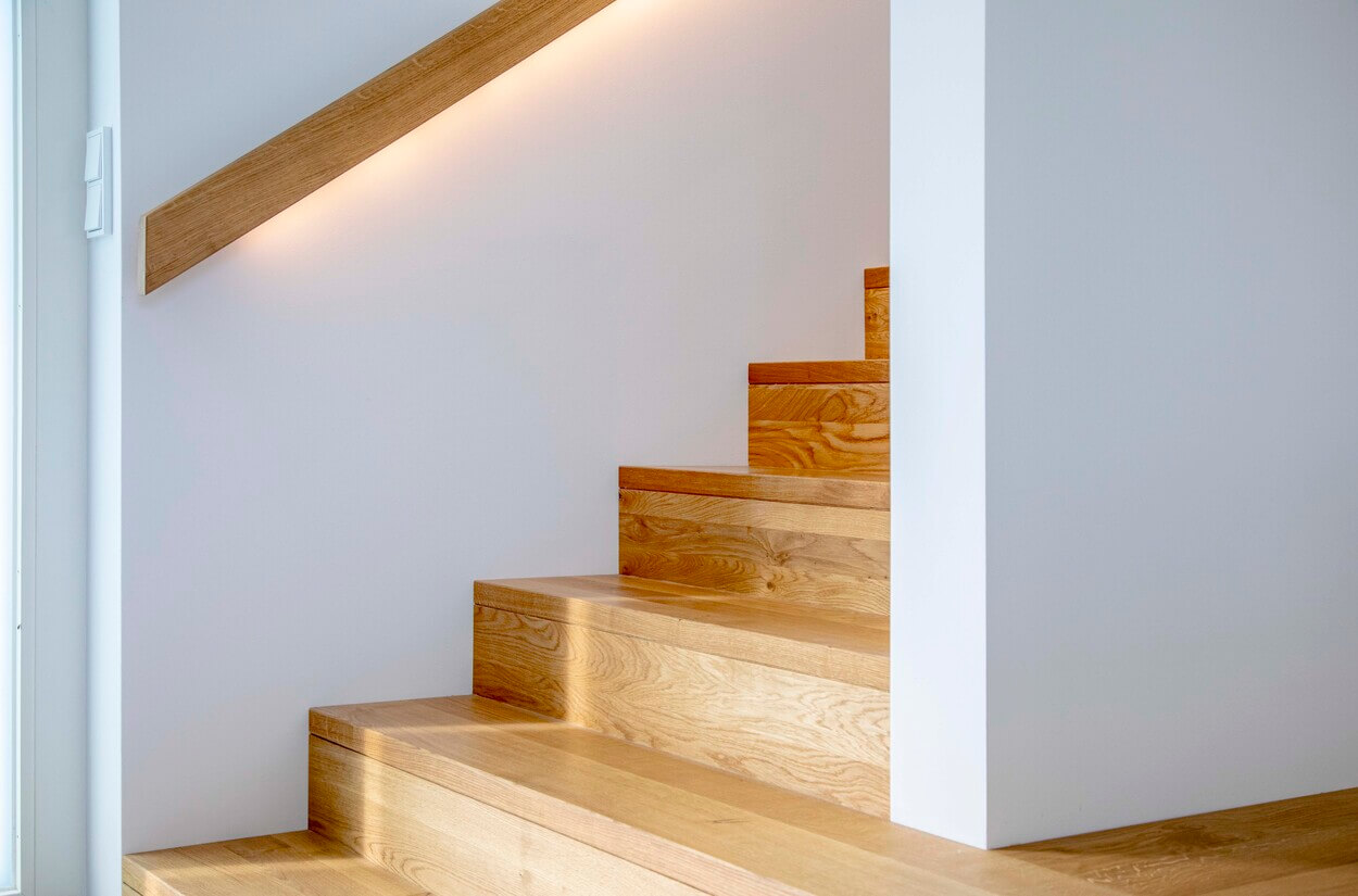 Die Holztreppe im Passivhaus Pliening besticht durch ihr elegantes, minimalistisches Design mit sanfter Wandbeleuchtung.