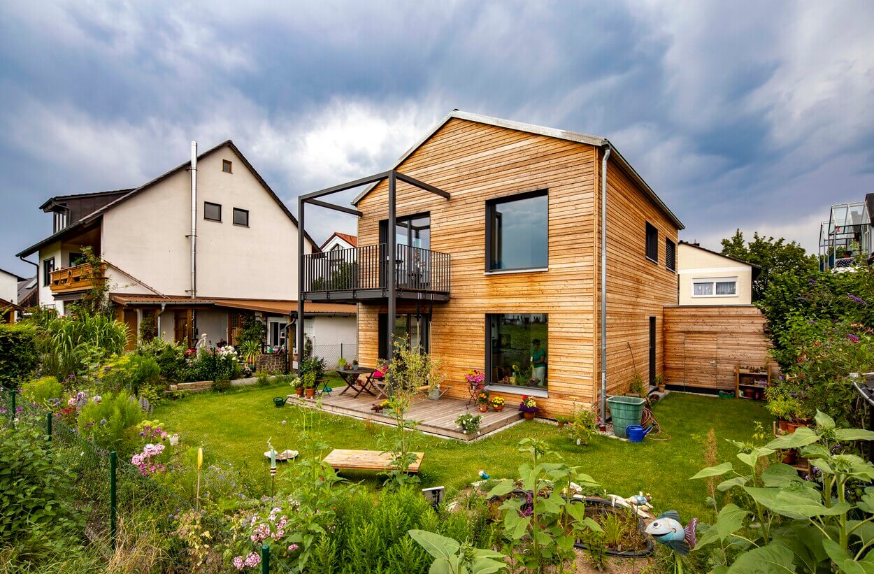 Ein modernes Holzhaus in Dachau mit gepflegtem Garten steht unter einem bewölkten Himmel.