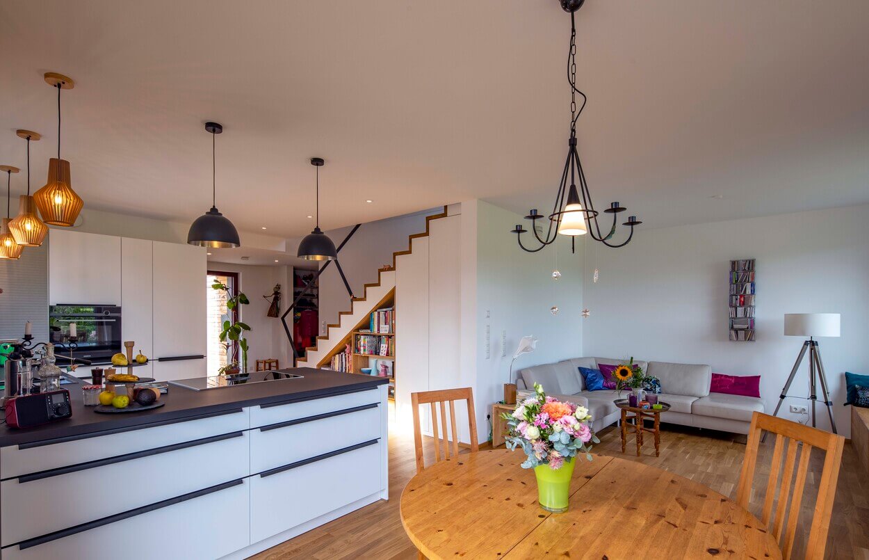 Der Essbereich eines modernen Holzhauses in Dachau zeigt einen einladenden Holztisch mit Blumen, eine Küche und eine gemütliche Sitzecke.