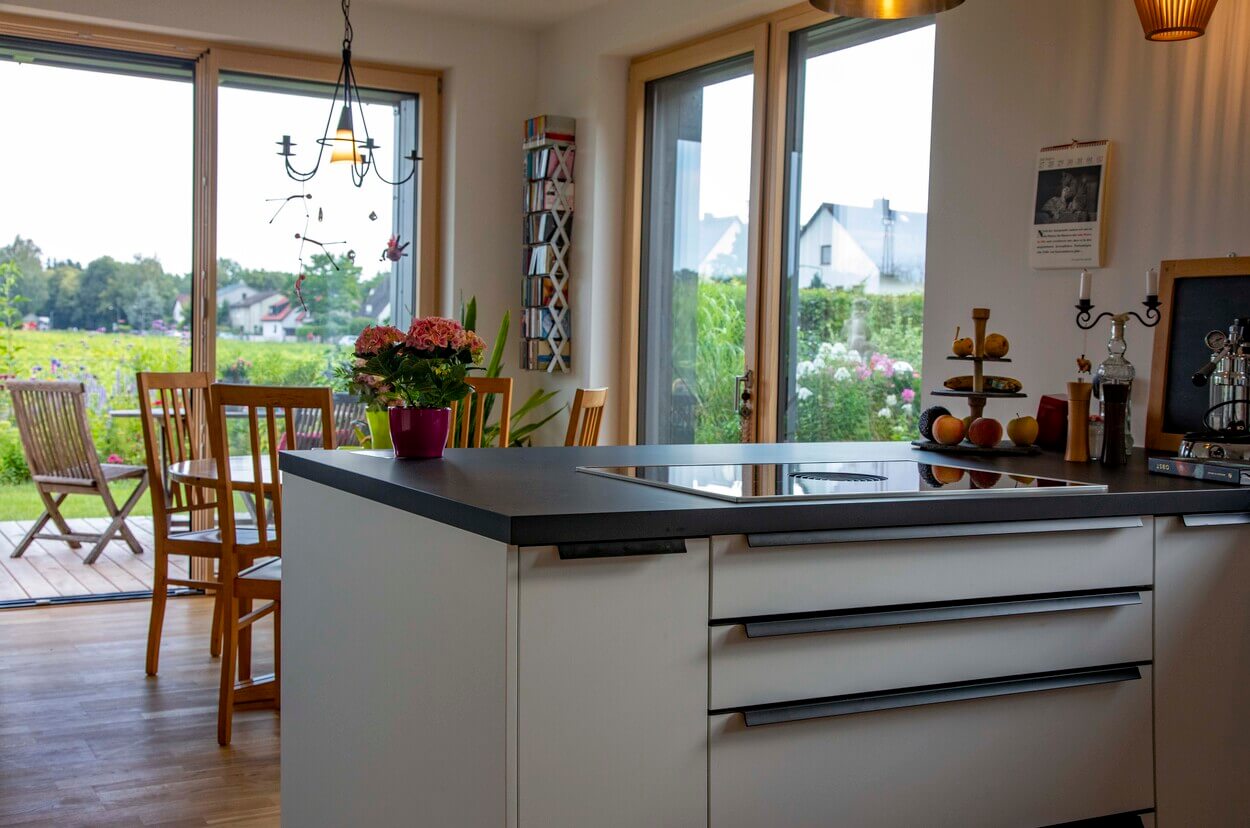 Eine moderne Küche mit Insel und Blumendekor bietet einen herrlichen Blick auf den grünen Garten durch große Fenster.