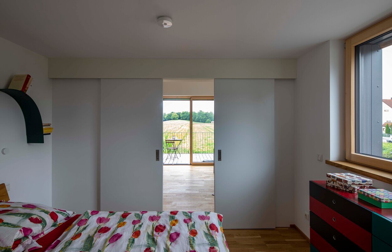 Ein Schlafzimmer mit Tulpenbettwäsche öffnet sich zu einem Balkon mit Aussicht auf ein grünes Feld in Dachau.