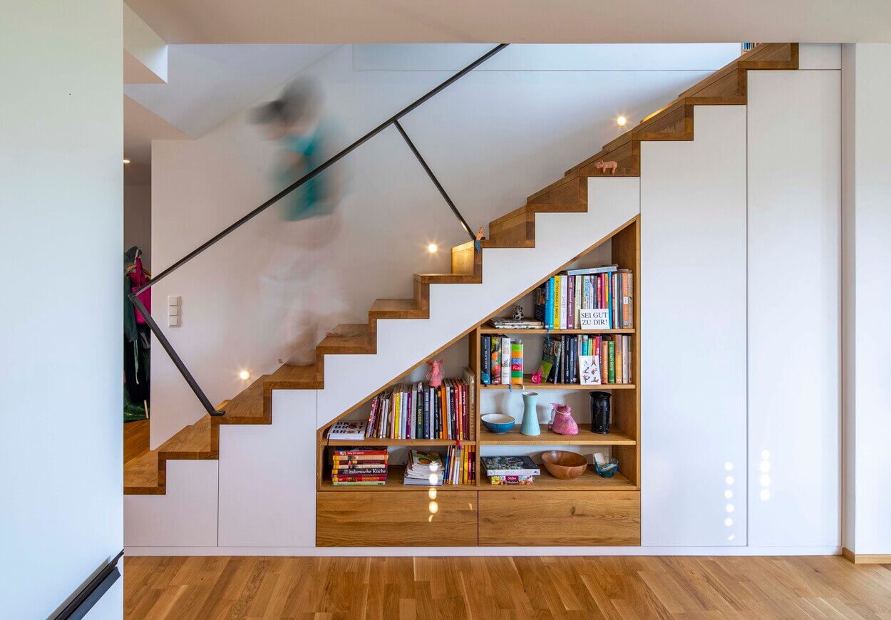 Eine Treppe in einem Holzhaus in Dachau integriert Stauraum mit ordentlich angeordneten Büchern und Dekorationen.