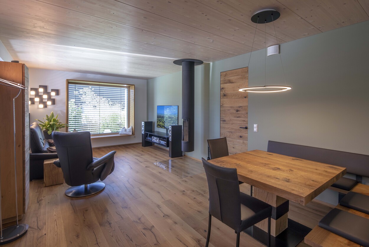 Ein modernes Wohnzimmer in Prien mit Holzdecke, Esstisch und einem gemütlichen Sessel am Fenster lädt zum Verweilen ein.