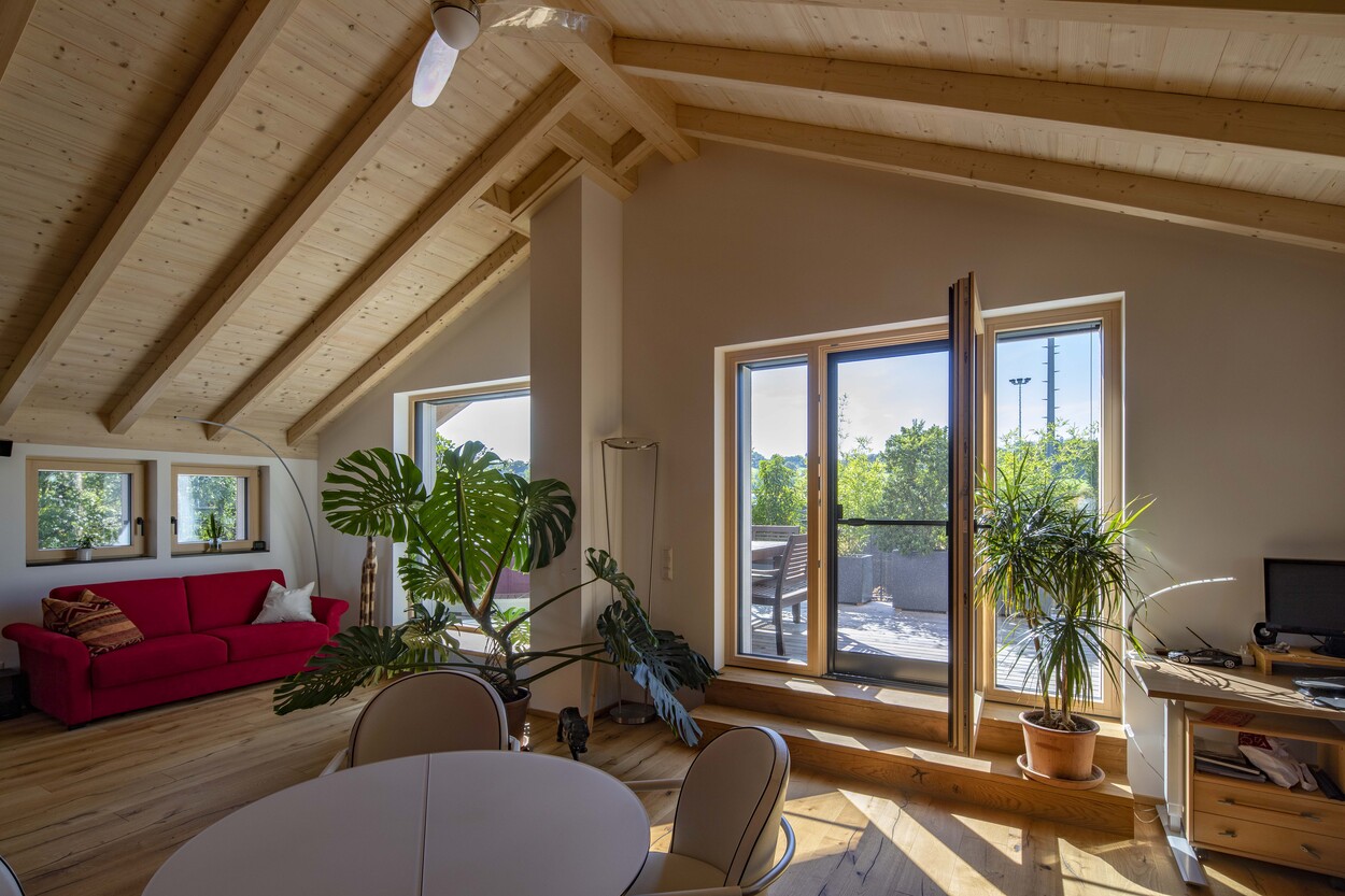 Ein helles Wohnzimmer in Prien mit rotem Sofa, Holzdecke und Blick auf die sonnige Terrasse eines Einfamilienhauses.