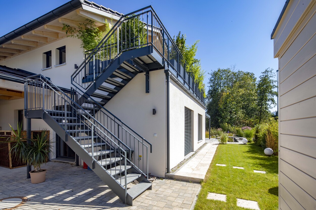 Ein modernes Einfamilienhaus in Prien glänzt im Sonnenlicht mit einer stilvollen Außentreppe und einem gepflegten Garten.