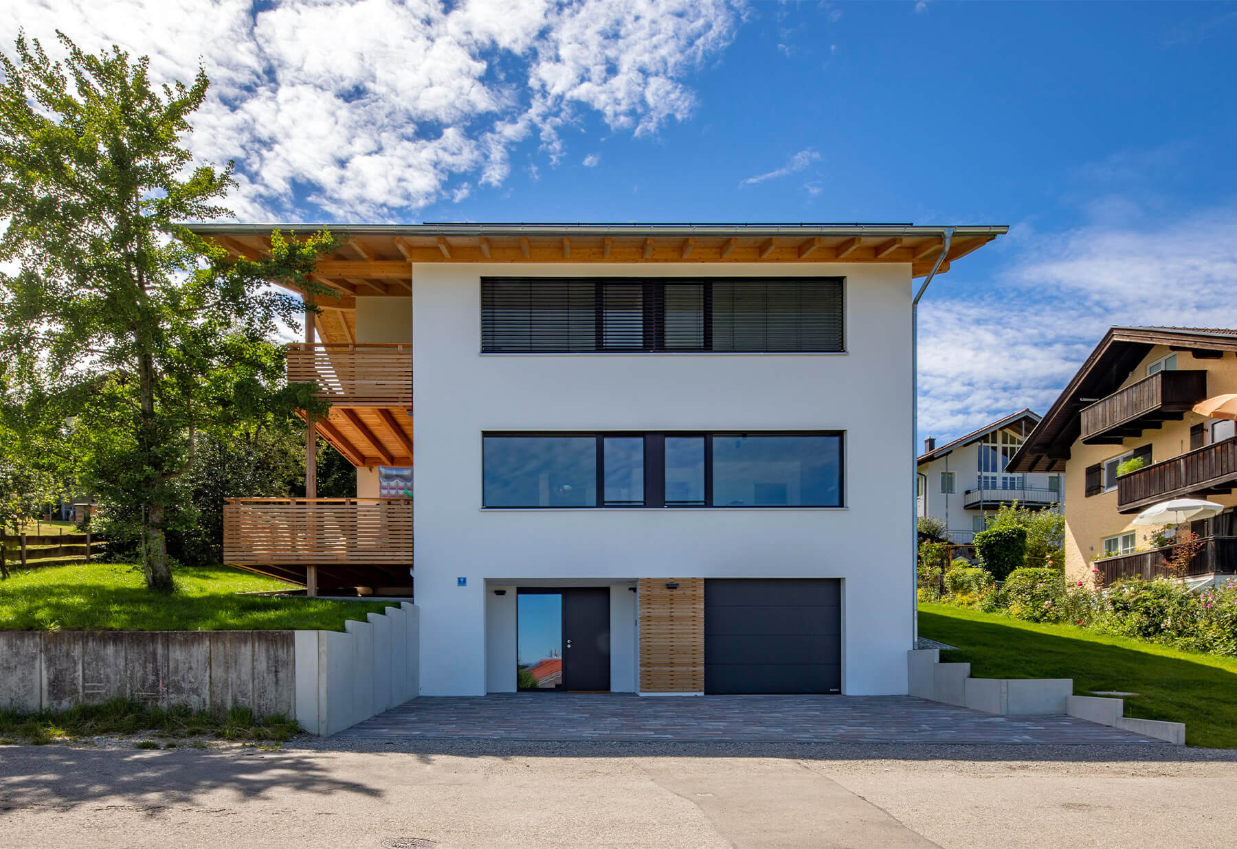 Modernes Holzhaus in Rimsting mit klarer Architektur, umgeben von grüner Landschaft unter strahlend blauem Himmel.