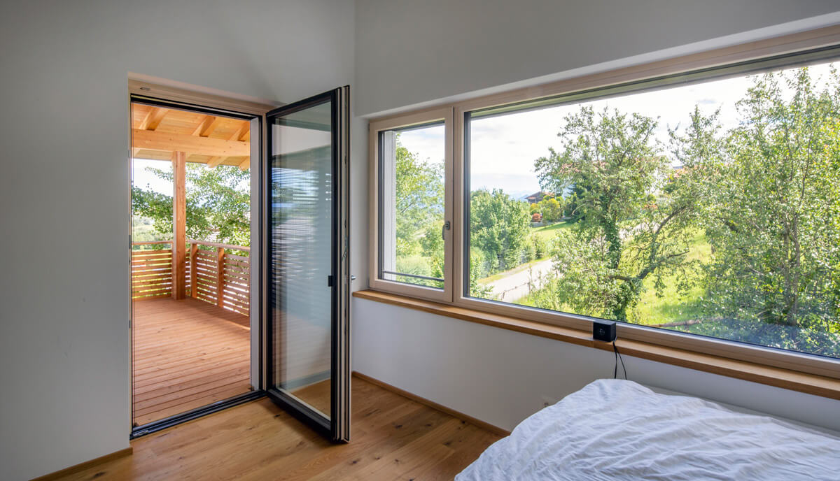 Ein gemütliches Schlafzimmer im Holzhaus in Rimsting bietet einen sonnigen Balkon mit Blick auf grüne Natur.