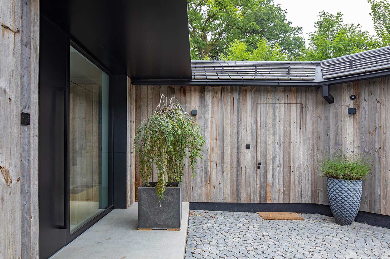 Ein moderner Innenhof mit Holzwänden, Glasfenstern und stilvollen Pflanzentöpfen schafft eine ruhige Atmosphäre.