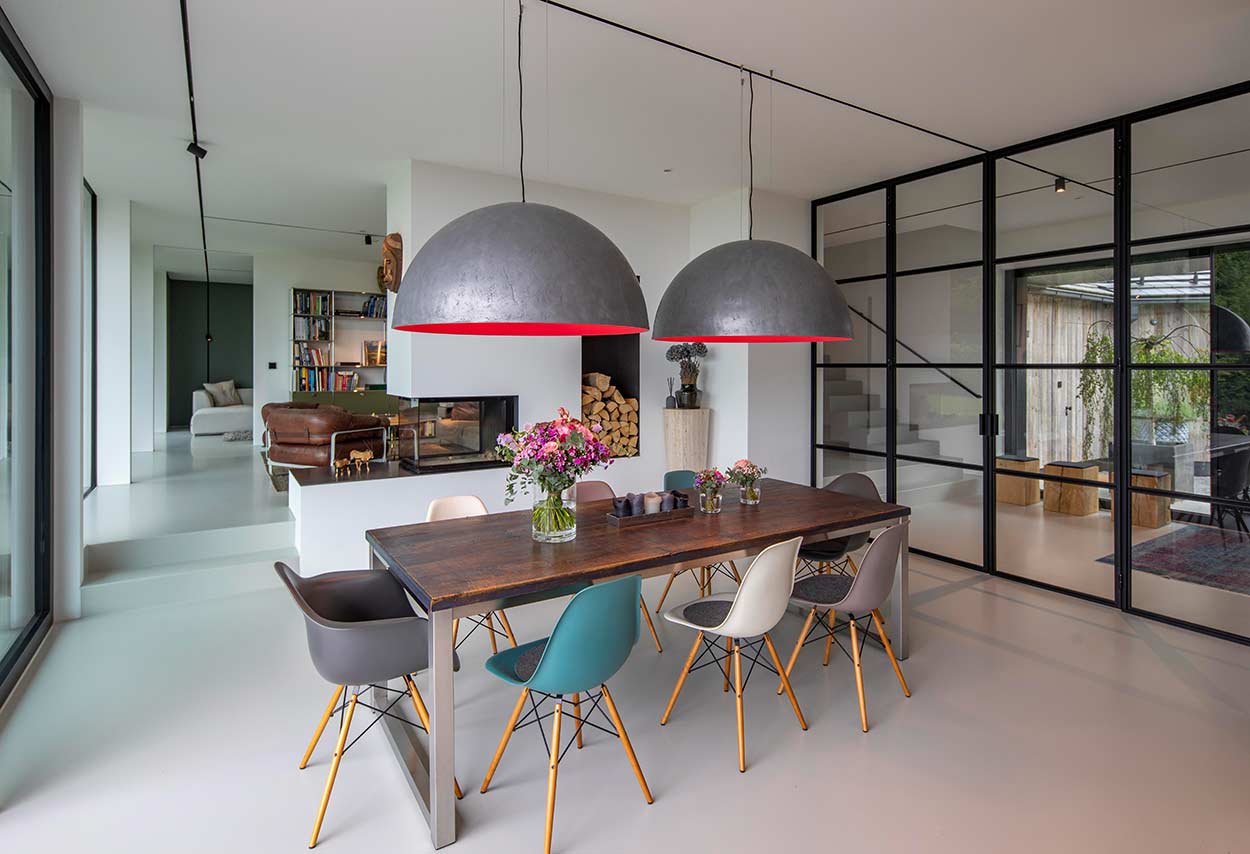 Ein moderner Essbereich mit Holztisch, bunten Stühlen und großen, grauen Pendelleuchten grenzt an ein elegantes Wohnzimmer.