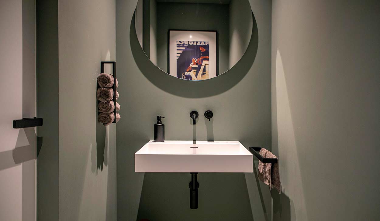 Ein modernes Badezimmer zeigt ein weißes Waschbecken mit rundem Spiegel und stilvoll gerollten Handtüchern an der Wand.