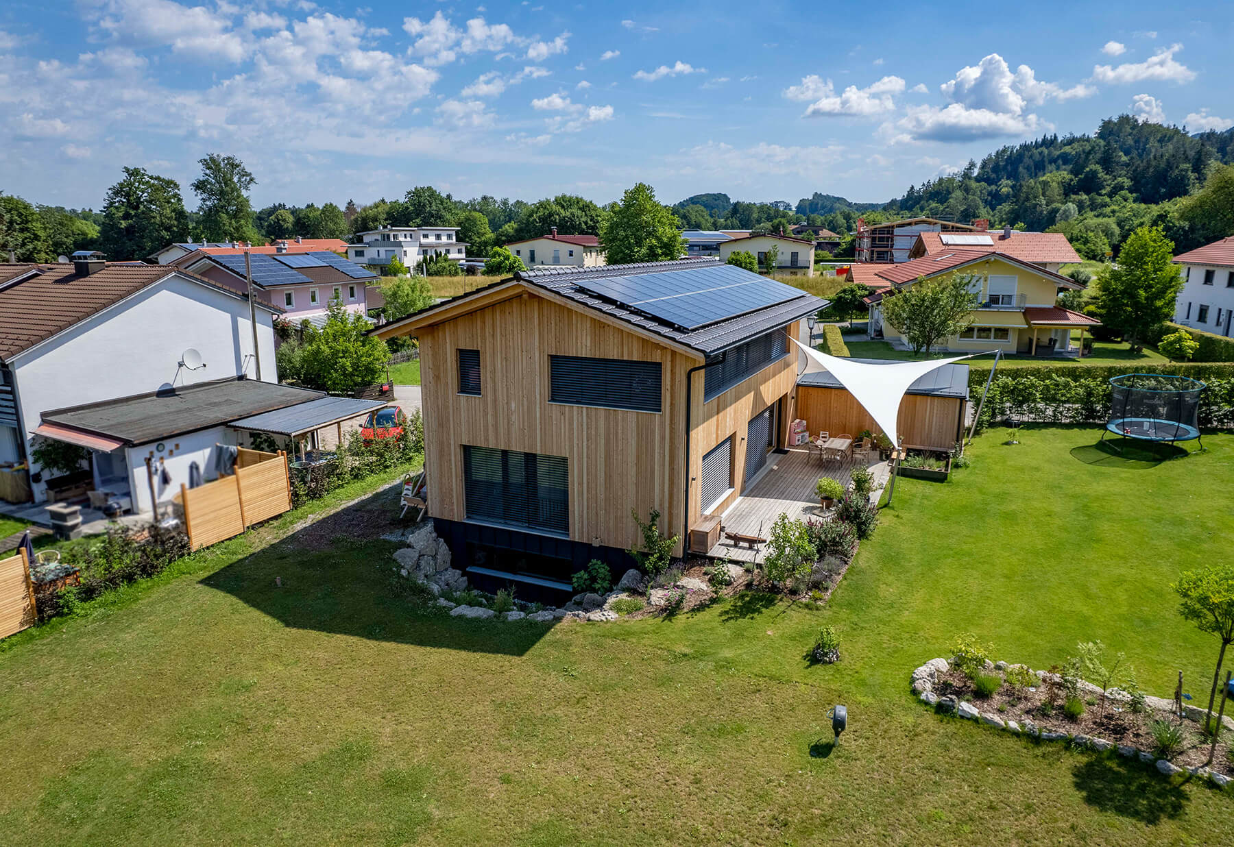 Ein modernes Holzhaus in Neubeuern mit Solarpanelen thront in einem grünen Garten unter strahlend blauem Himmel.