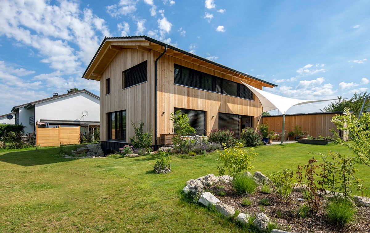 Ein modernes Holzhaus in Neubeuern steht in einem gepflegten Garten unter blauem Himmel.
