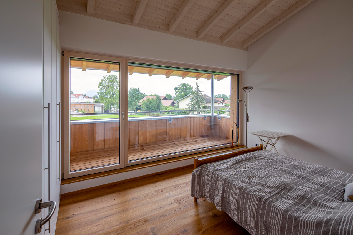 Ein gemütliches Schlafzimmer im Holzhaus in Chieming bietet durch große Fenster einen Blick auf den Balkon und die Umgebung.