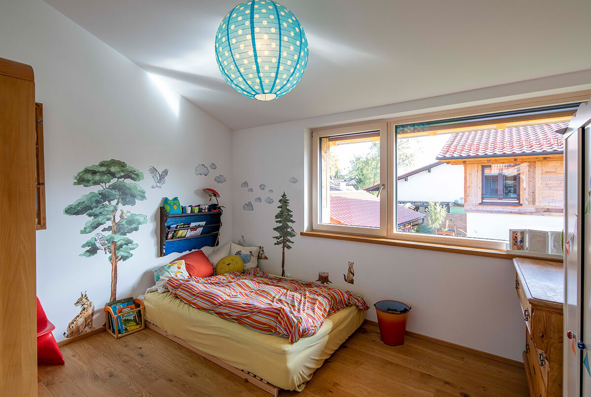 Ein Kinderzimmer in einem Holzhaus in Oberbiberg zeigt bunte Wandmalereien und ein großes Fenster mit Ausblick nach draußen.