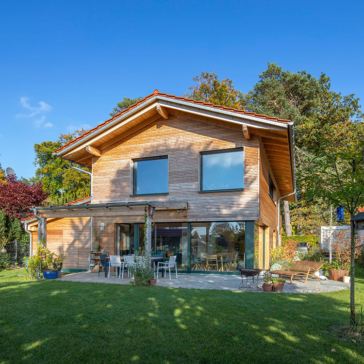 Ein modernes Holzhaus in Oberbiberg steht bei sonnigem Wetter inmitten eines grünen Gartens.