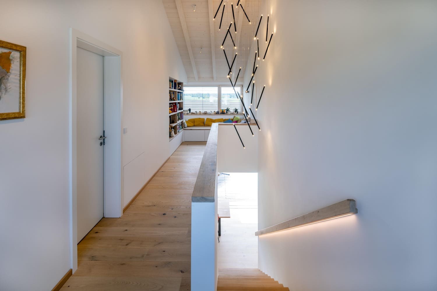 Holzhaus in Weilheim, hier Trepenhaus und Flur im OG, Treppengeländer beleuchtet, weißlasierter Dachstuhl