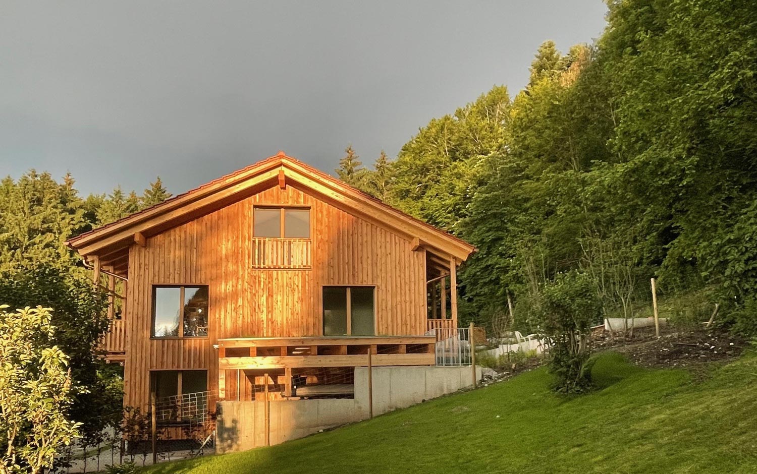 Holzhaus Miesbach, Mehrfamilienhaus am Hang, Holzfassade, Stirn Holzbauweise, Abendlicht