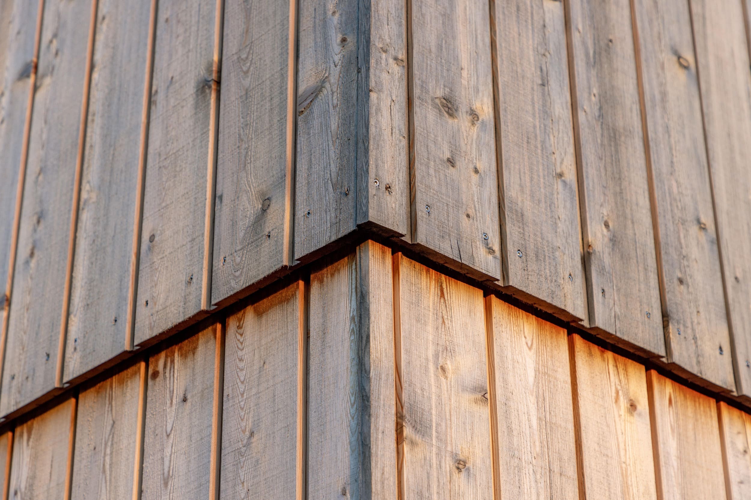Holzverkleidungen bilden eine stilvolle Ecke eines Gebäudes und werden von warmem Sonnenlicht beleuchtet.