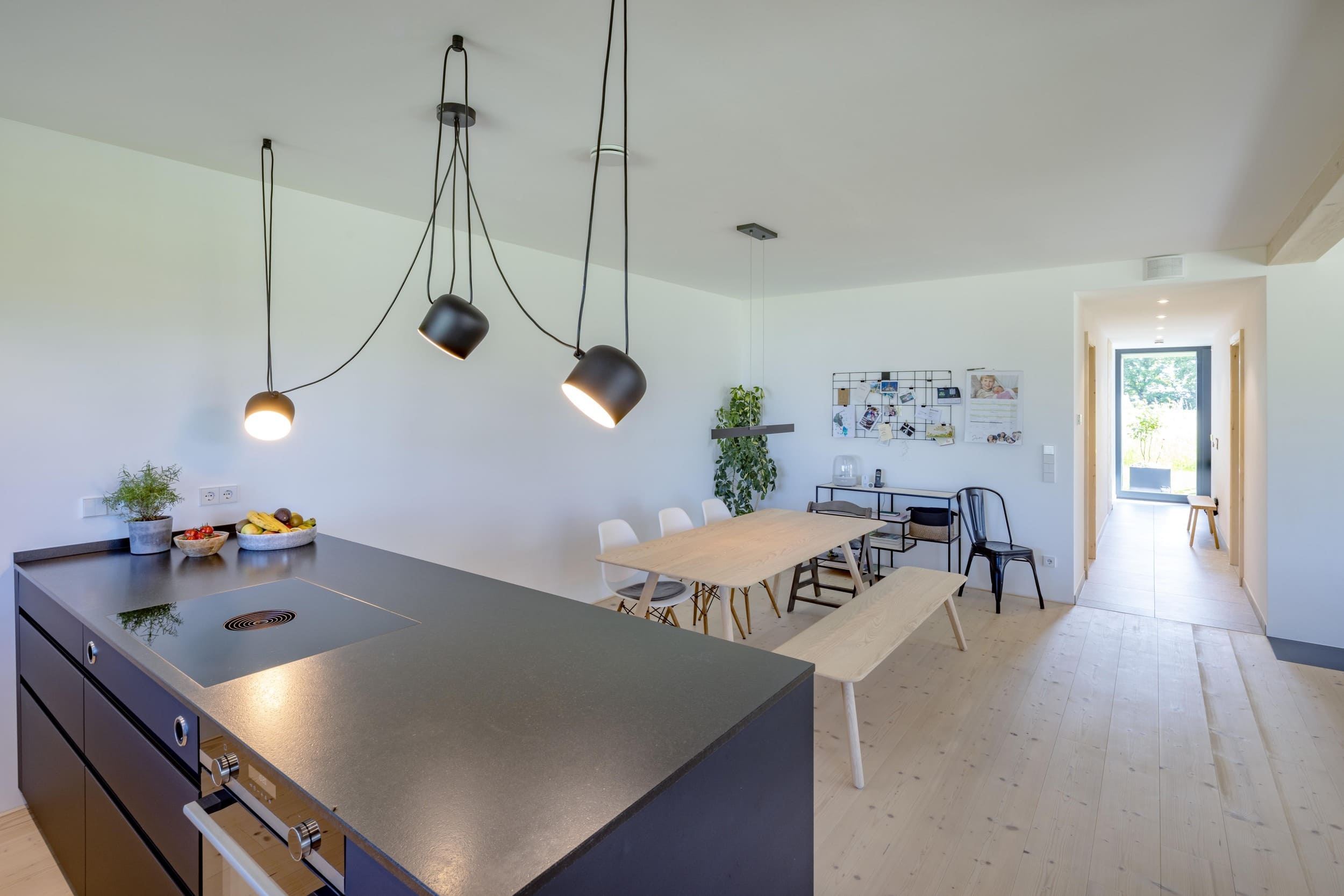 Eine moderne Küche mit schwarzer Arbeitsplatte und stilvollen Hängelampen öffnet sich zu einem hellen Essbereich.