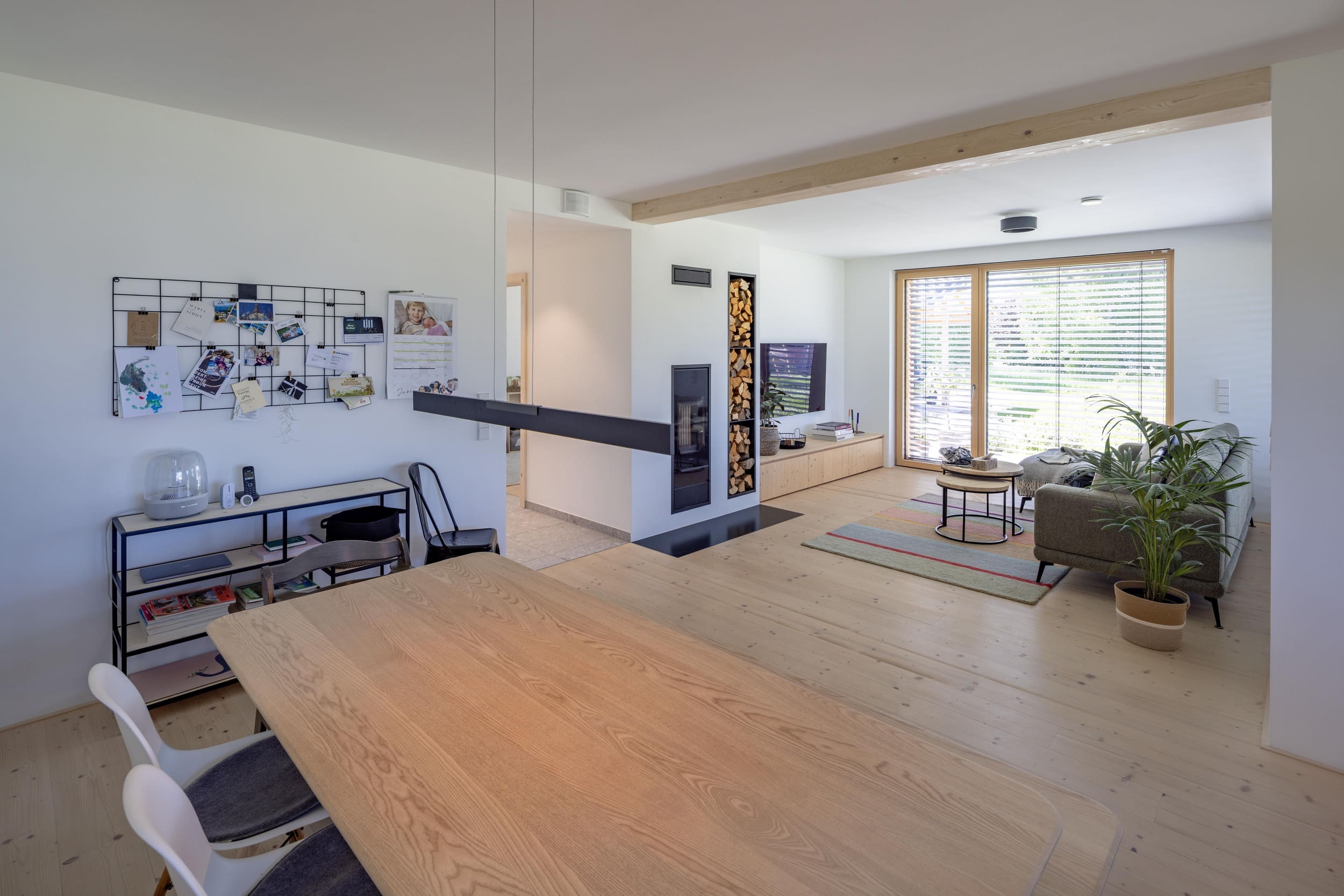 Ein modernes Wohnzimmer mit Holzboden, einem großen Esstisch und einem gemütlichen Sofa vor großen Fenstern.