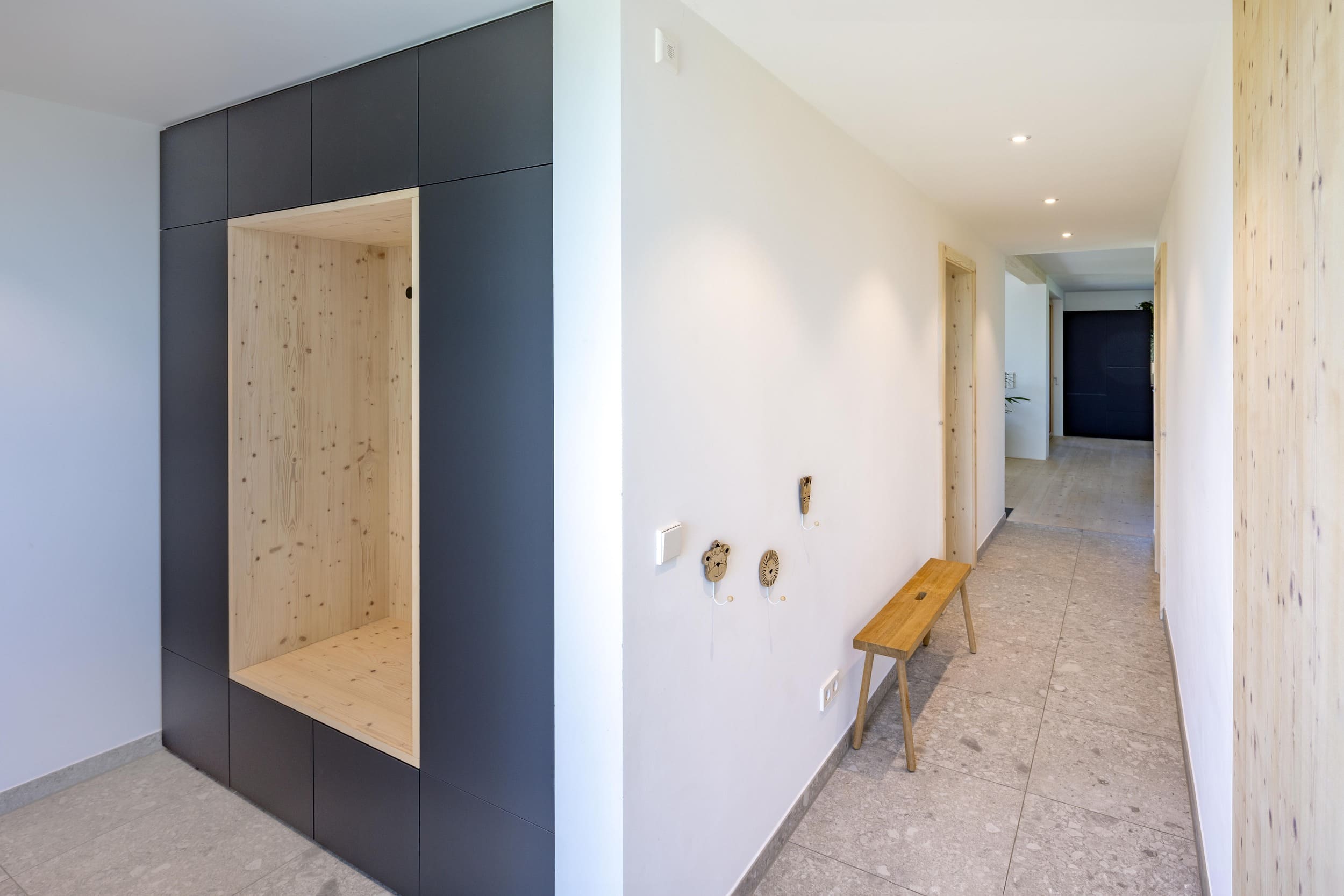 Ein moderner Flur zeigt einen hellen Holzeinbau und eine minimalistische Holzbank auf grauem Fliesenboden.