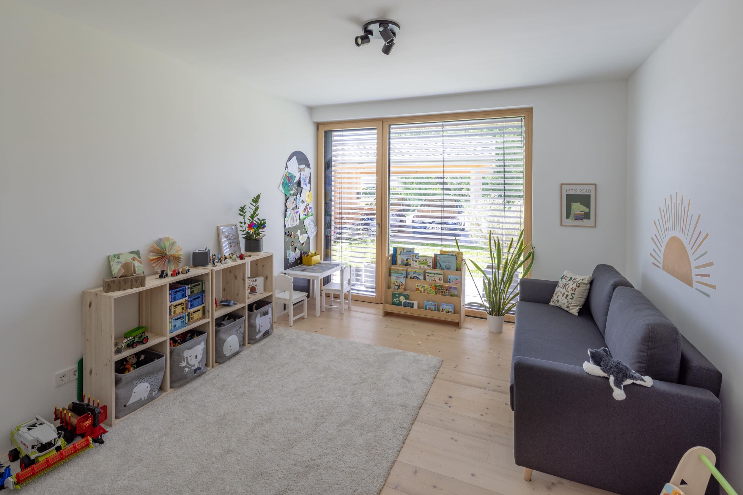 Ein helles Kinderzimmer mit Spielzeugregal, gemütlichem Sofa und großen Fenstern lädt zum Spielen und Entspannen ein.