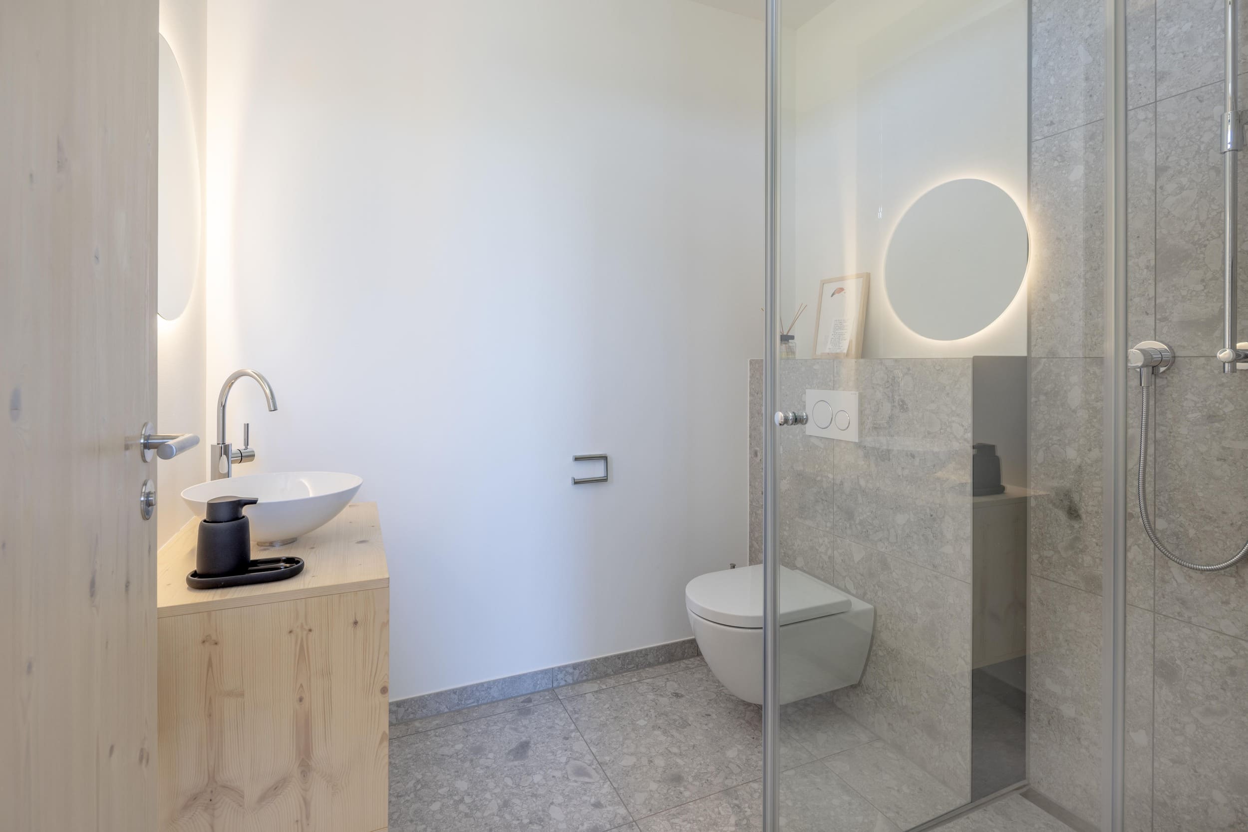 Ein modernes Badezimmer mit Glasdusche, beleuchtetem Spiegel und hölzernem Waschtisch strahlt zeitlose Eleganz aus.