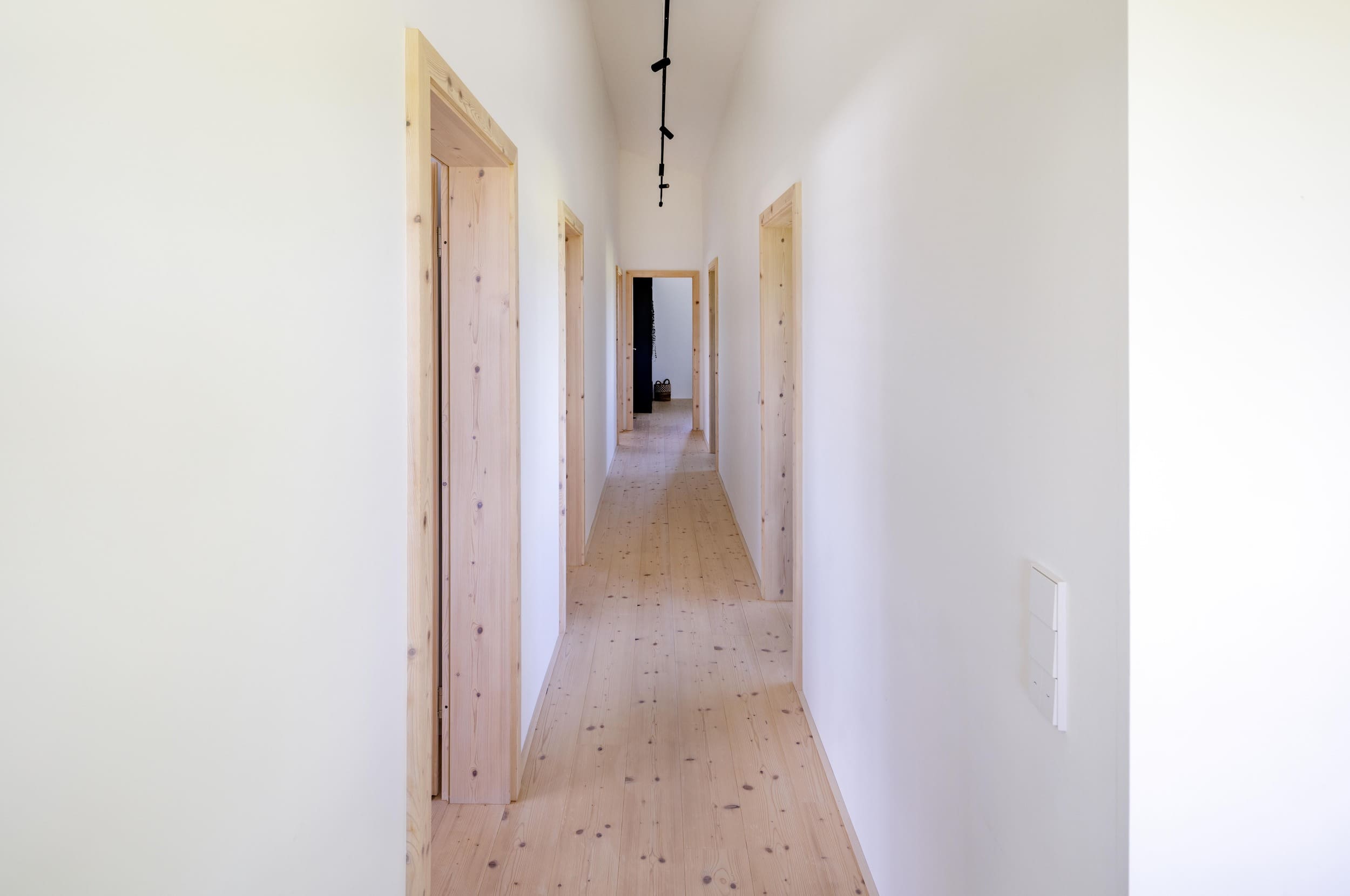 Ein langer, heller Flur mit minimalistischer Decke und Holztüren führt zu einem entfernten Raum.