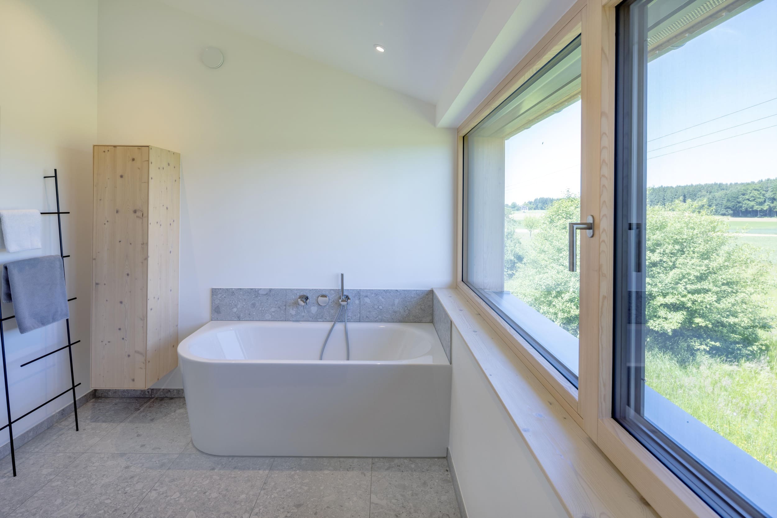 Ein modernes Badezimmer mit Badewanne und großem Fenster bietet einen herrlichen Blick auf die grüne Landschaft.